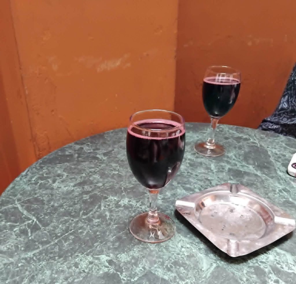 2 small glasses of red wine on a table with an empty ashtray between them